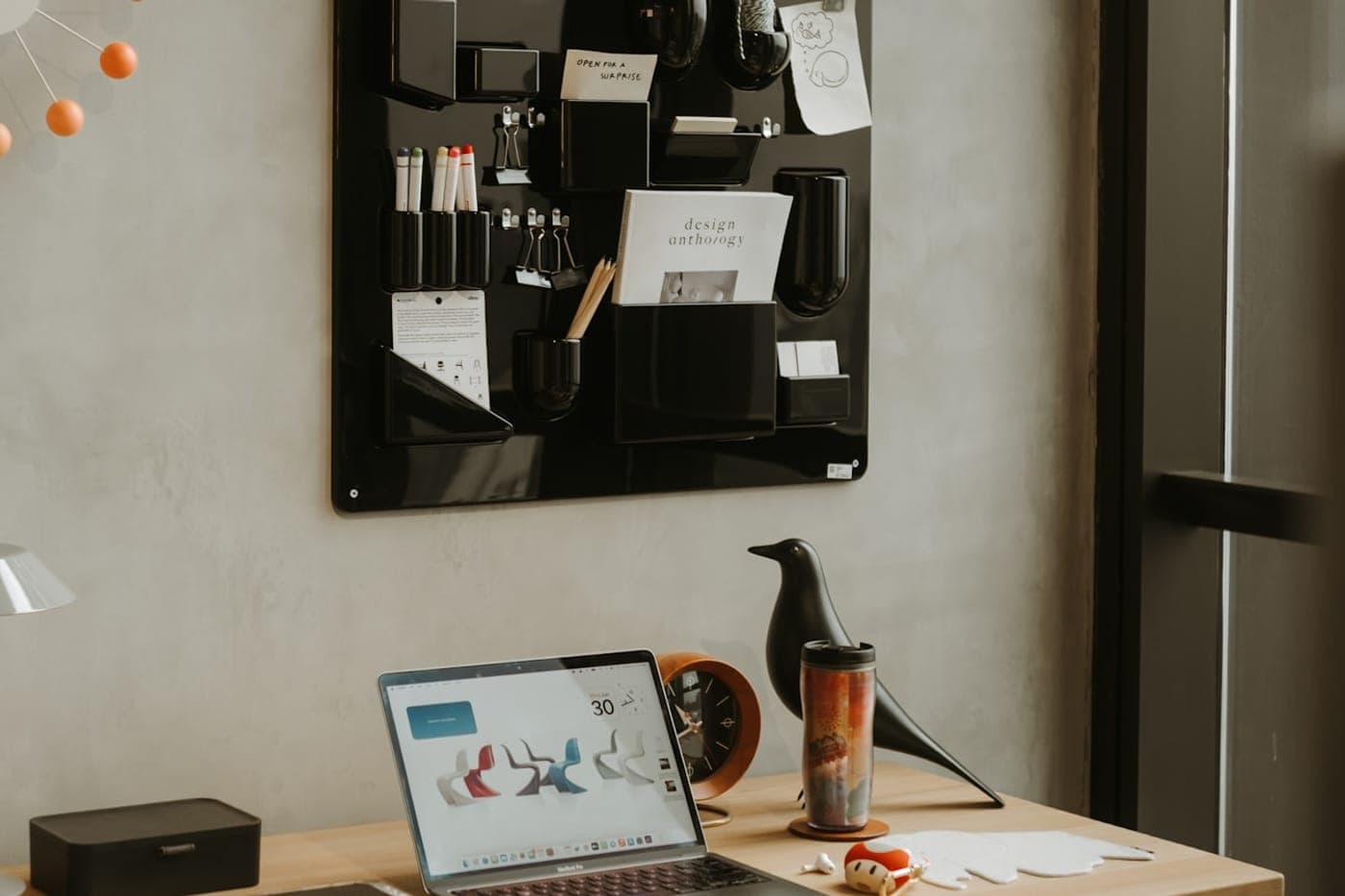 Tidy modern desk with a laptop, design objects and a wall organizer in a calm warm-lit workspace