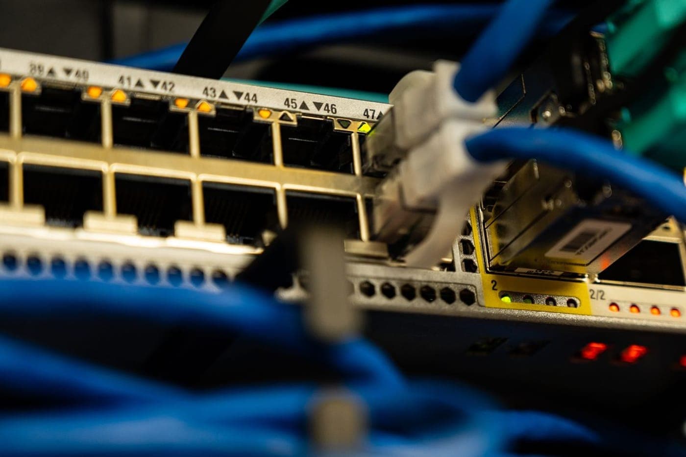 Teal fiber optic cables flowing from a network switch in a dark rack