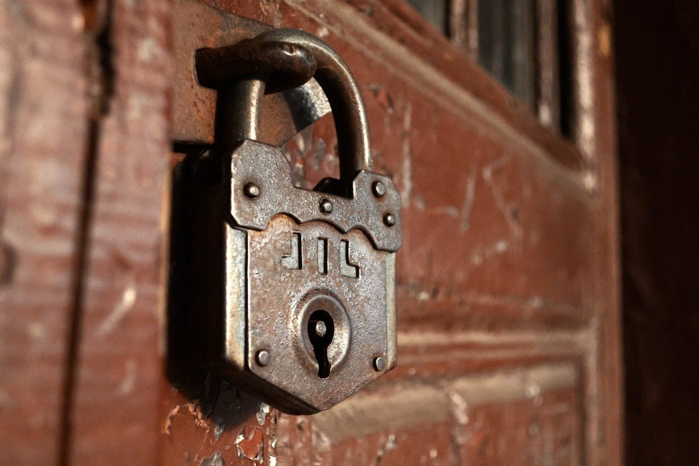Aged iron padlock locked on a weathered rust-red wooden door
