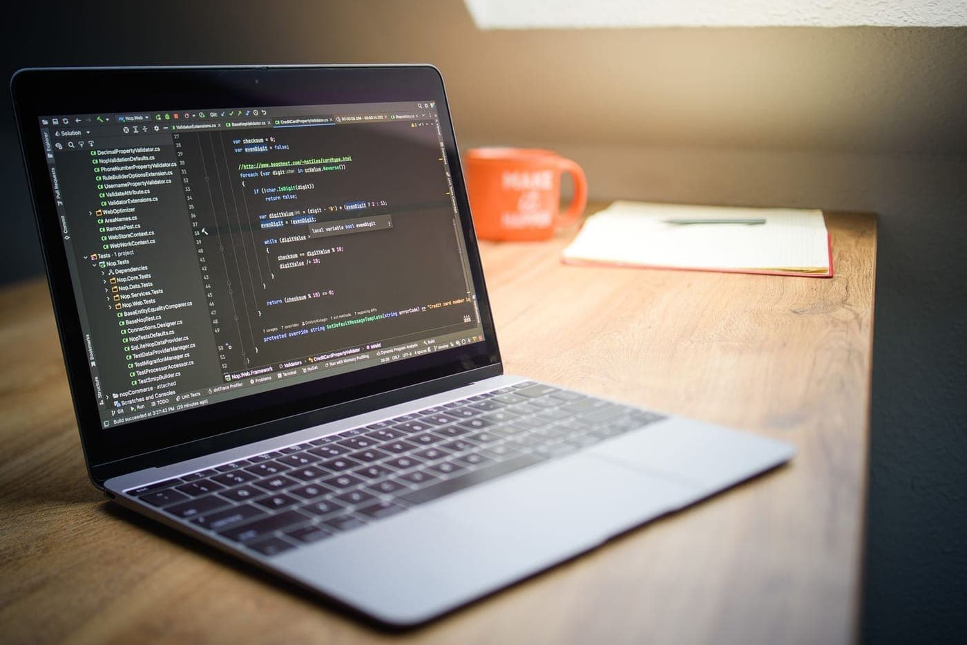 Laptop showing a code editor on a warm wooden desk with an orange mug in soft light