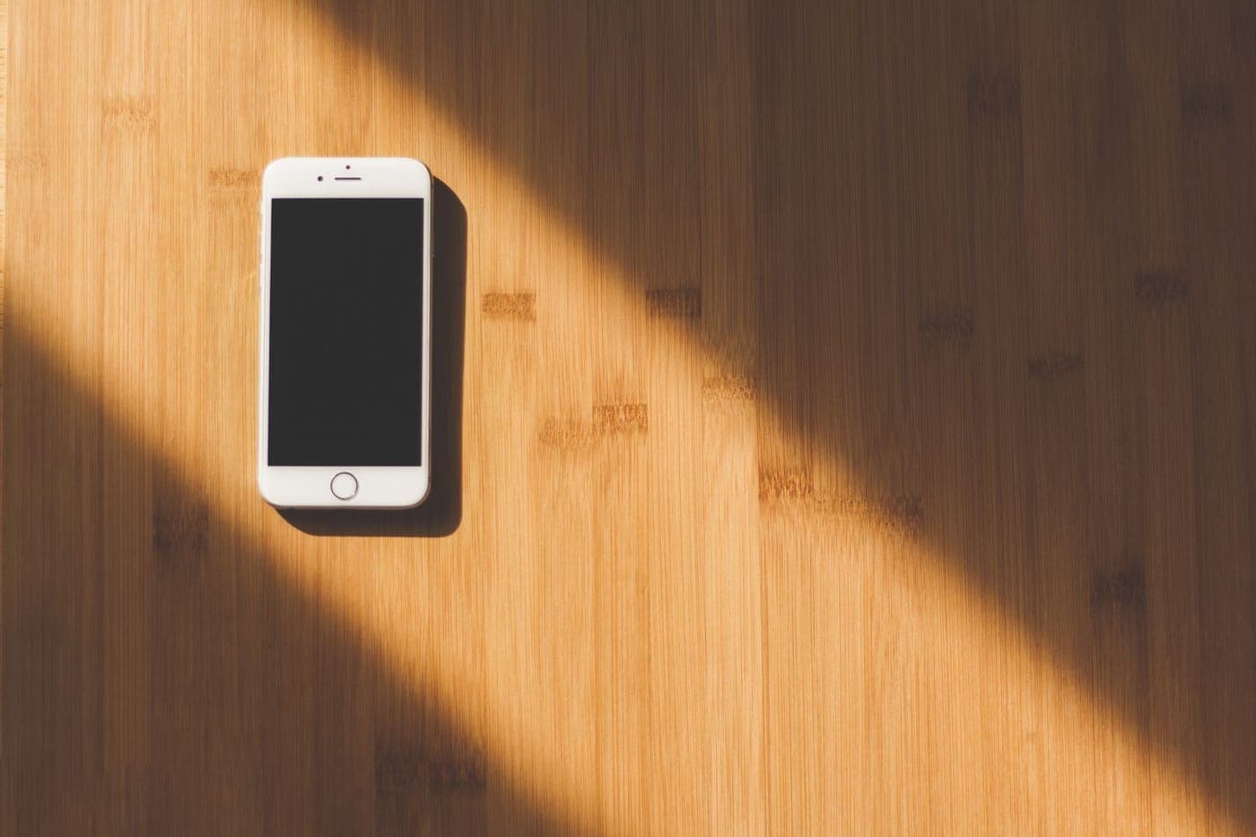 White smartphone on a bamboo surface crossed by a diagonal beam of sunlight