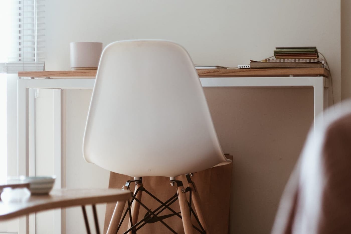 An empty white chair at a calm minimal desk by a window in warm cream and wood tones