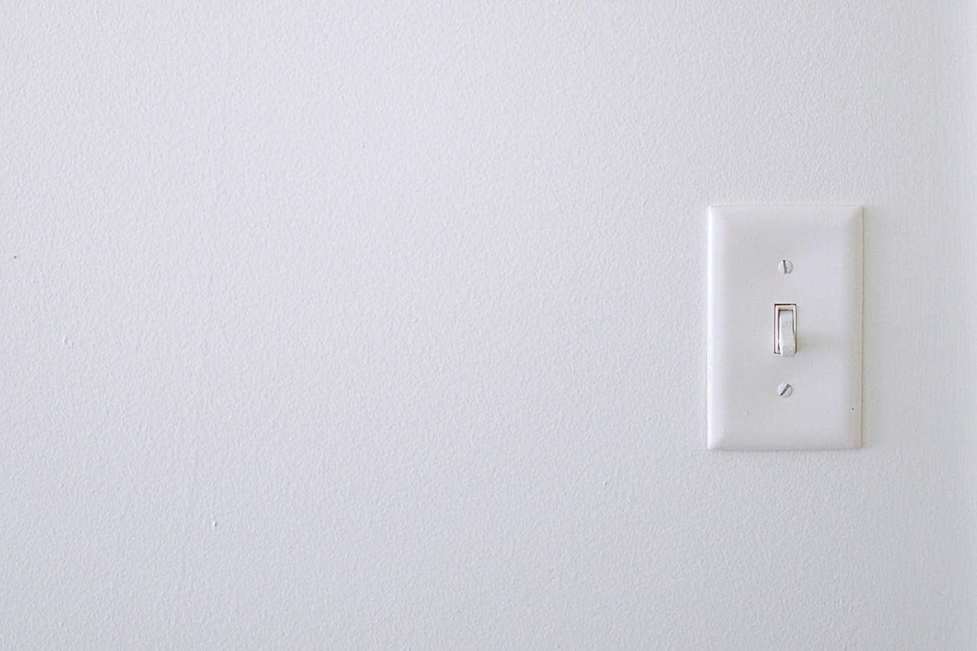 A single white toggle light switch on a clean white wall with generous negative space