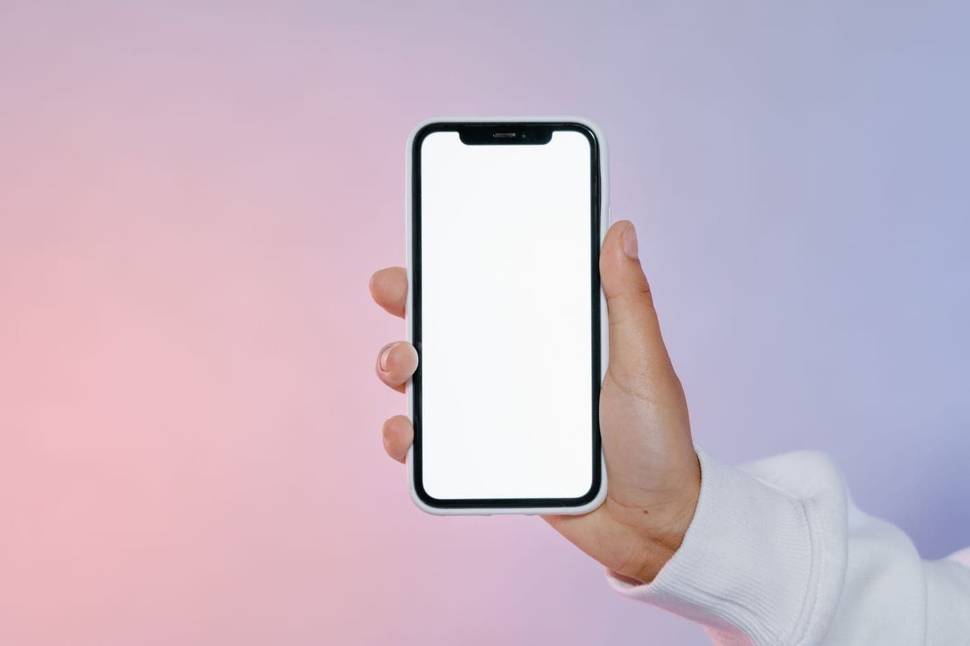 A hand holding a modern smartphone with a blank screen against a soft gradient
