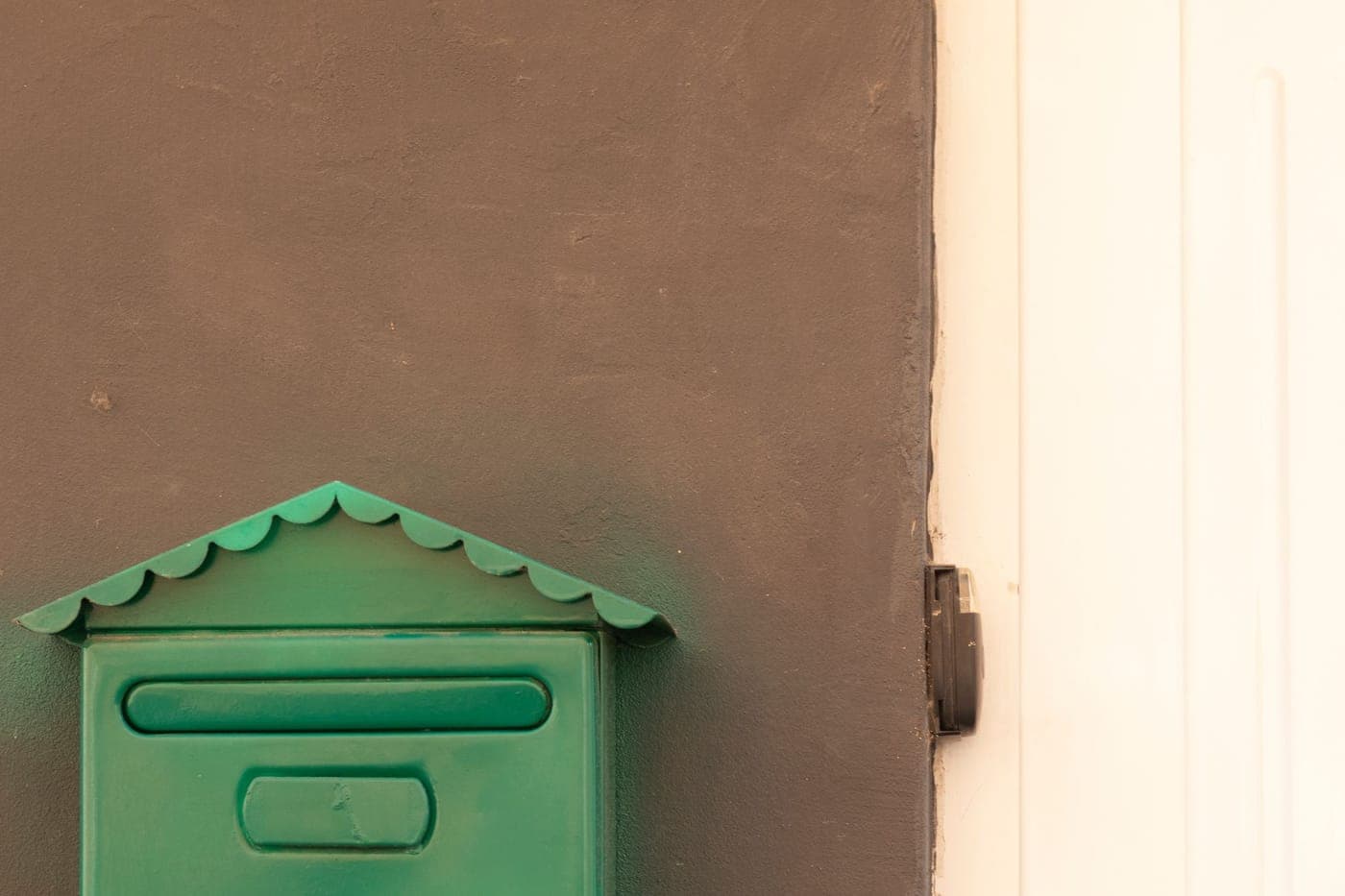 A green wall-mounted mailbox beside a white door
