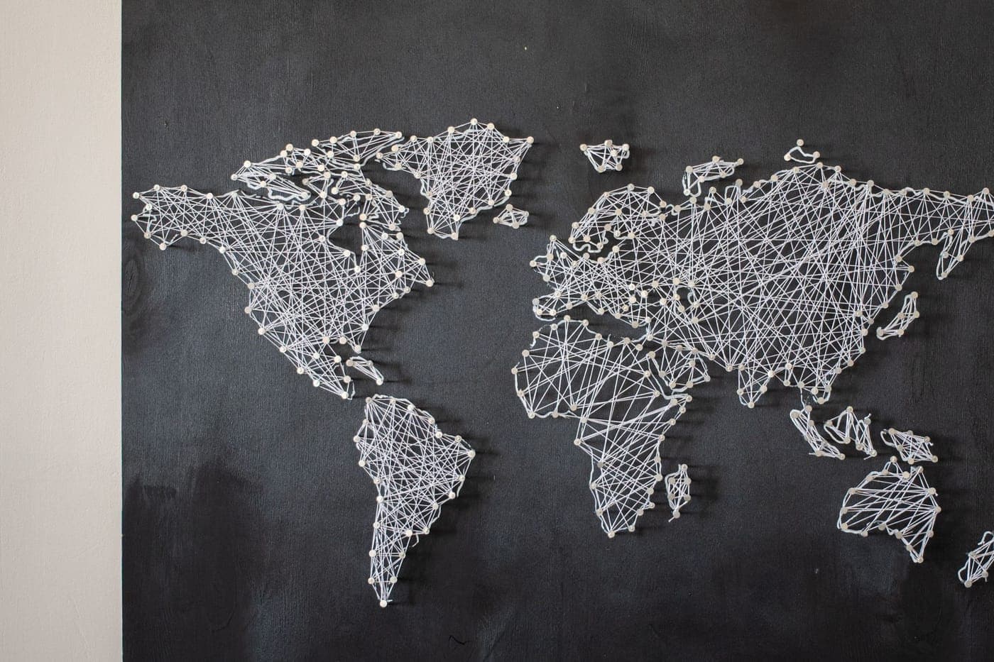 String art of a world map made of connected threads on a dark board