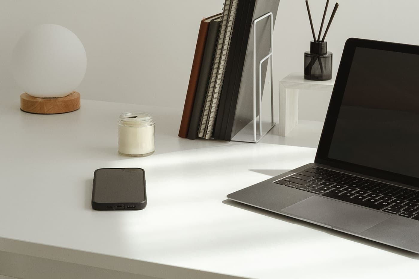 Minimal white desk with a laptop, phone and notebooks