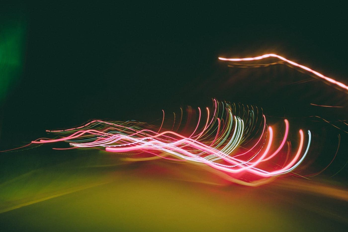Abstract long-exposure pink and green light streaks against darkness