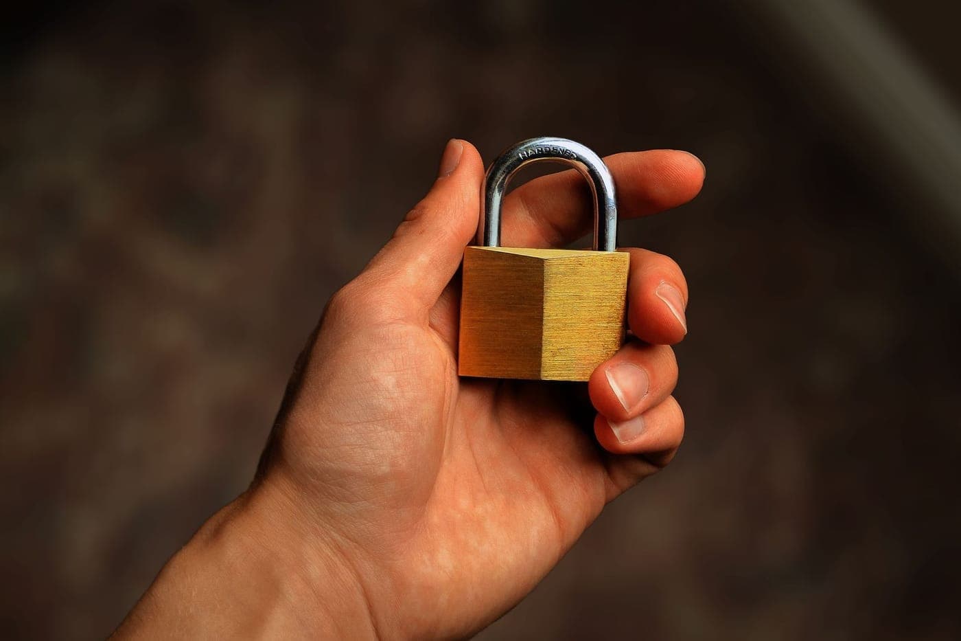 A hand holding a brass padlock against a soft dark warm background