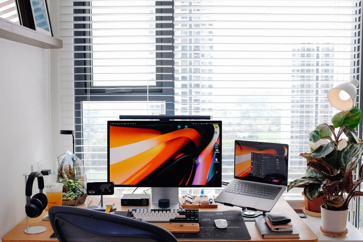 Clean modern desk setup with a monitor, laptop and plants beside a bright window