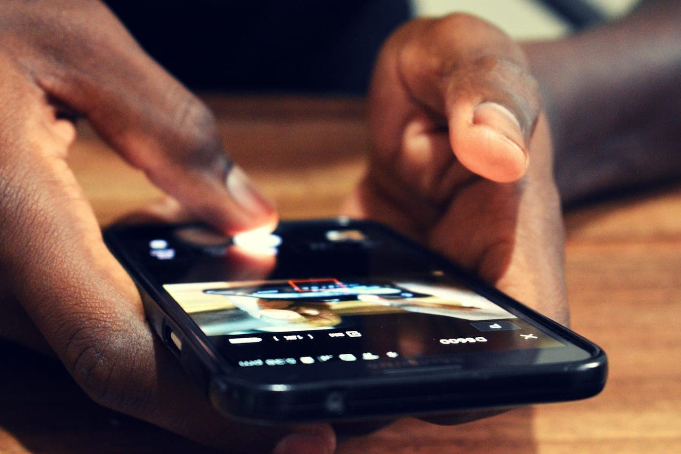 Close-up of hands tapping a smartphone screen resting on a warm wooden table