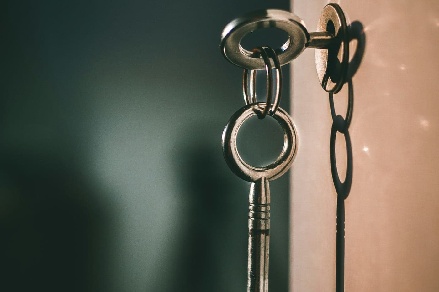 Elegant silver skeleton key on a ring casting a soft shadow against a muted teal and cream wall