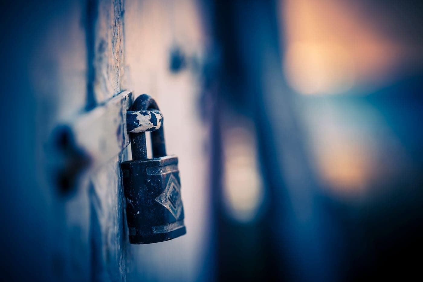 A real metal padlock in sharp focus against a soft blue and warm bokeh background