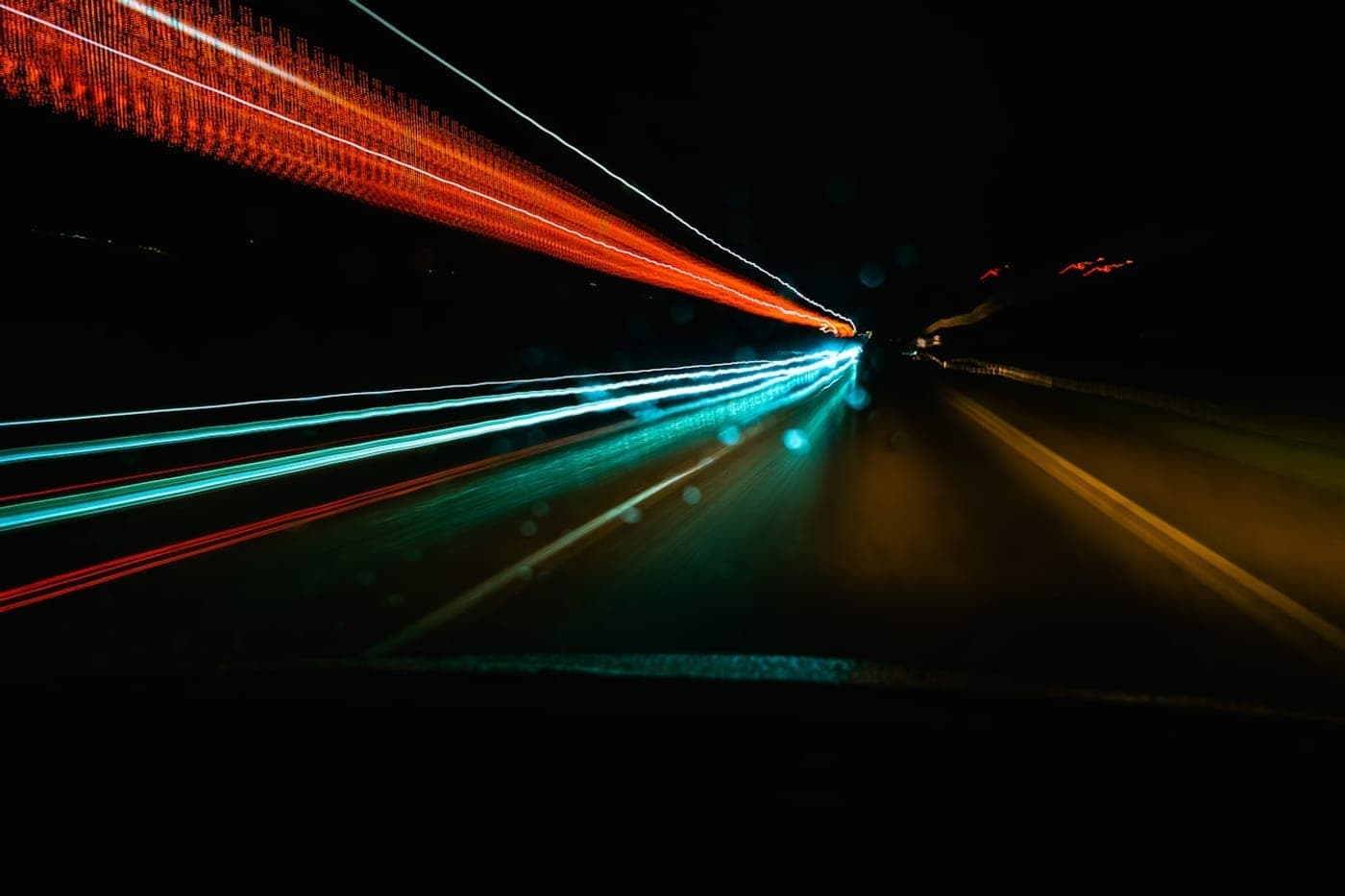 Long-exposure light trails rushing forward along a dark night road