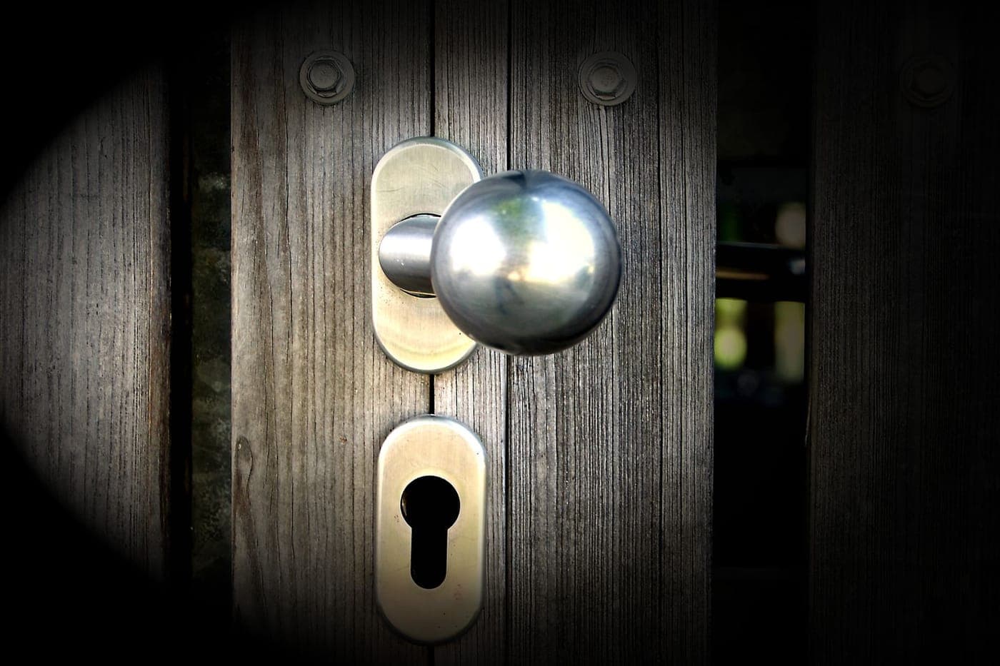 Close-up of a metal door knob and keyhole on a weathered wooden door