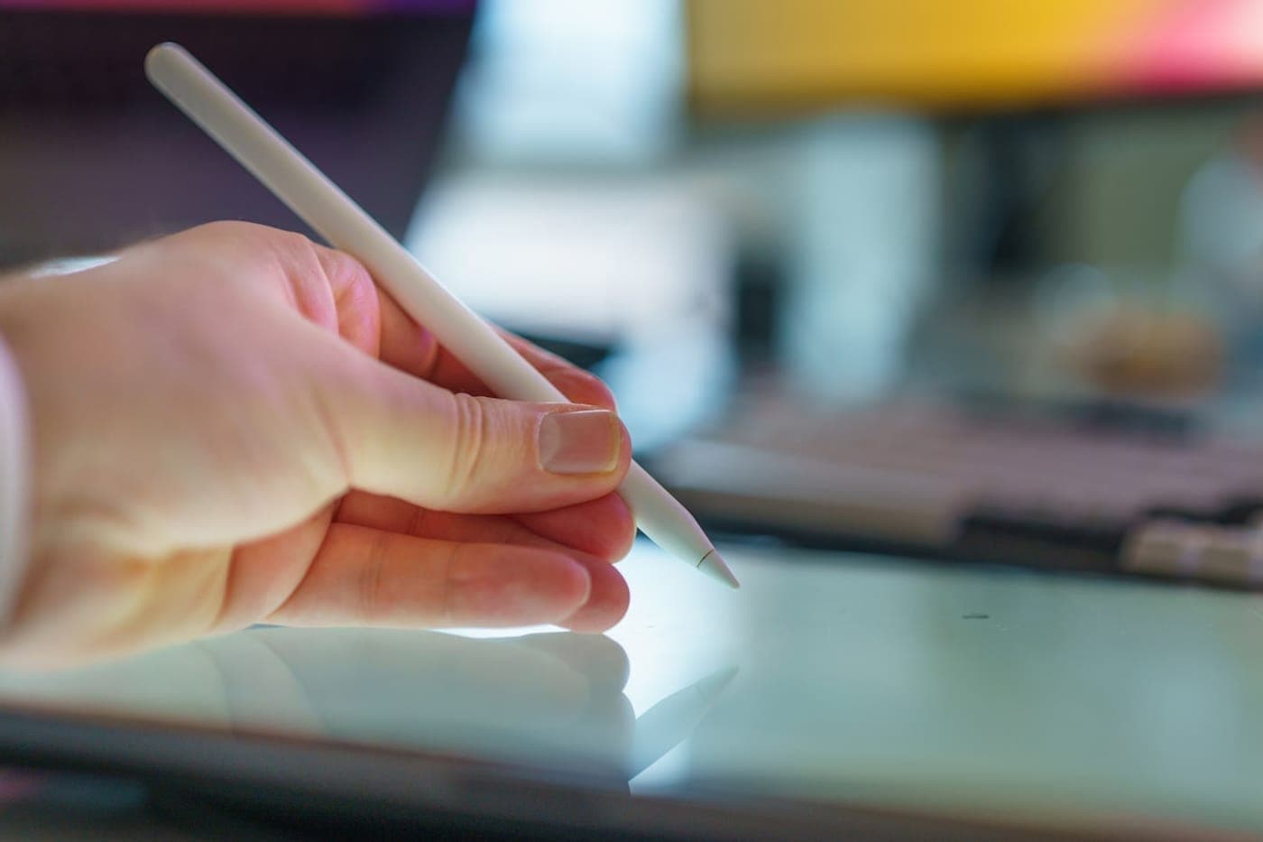 A hand using a stylus on a tablet at a warm creative design desk