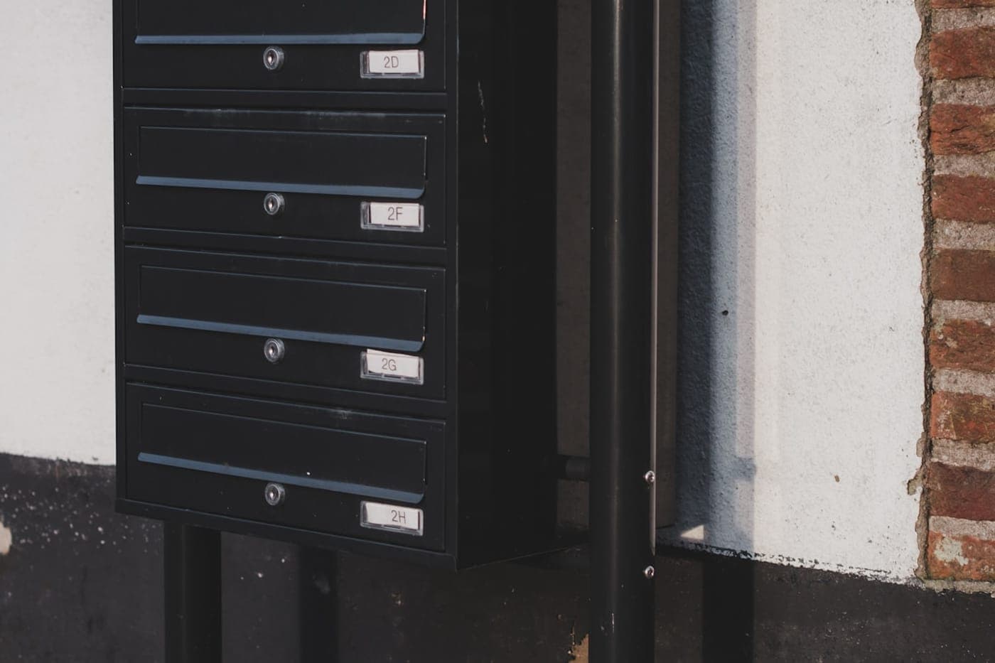A row of modern black multi-unit mailboxes mounted outside a building in warm daylight