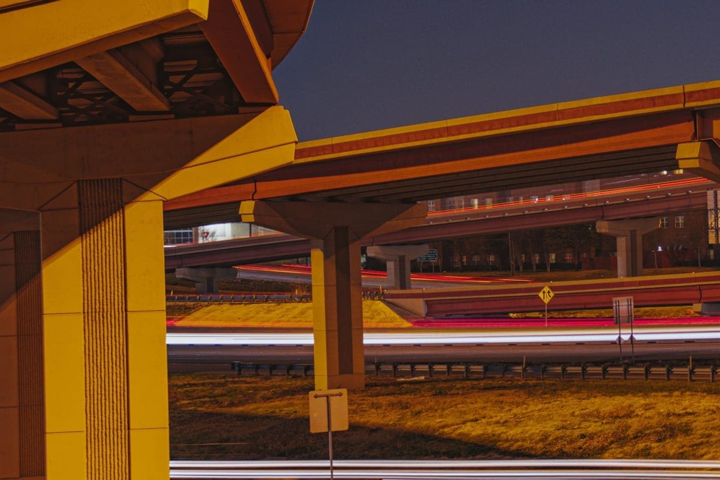 Long-exposure light trails under a highway interchange at dusk in warm amber tones