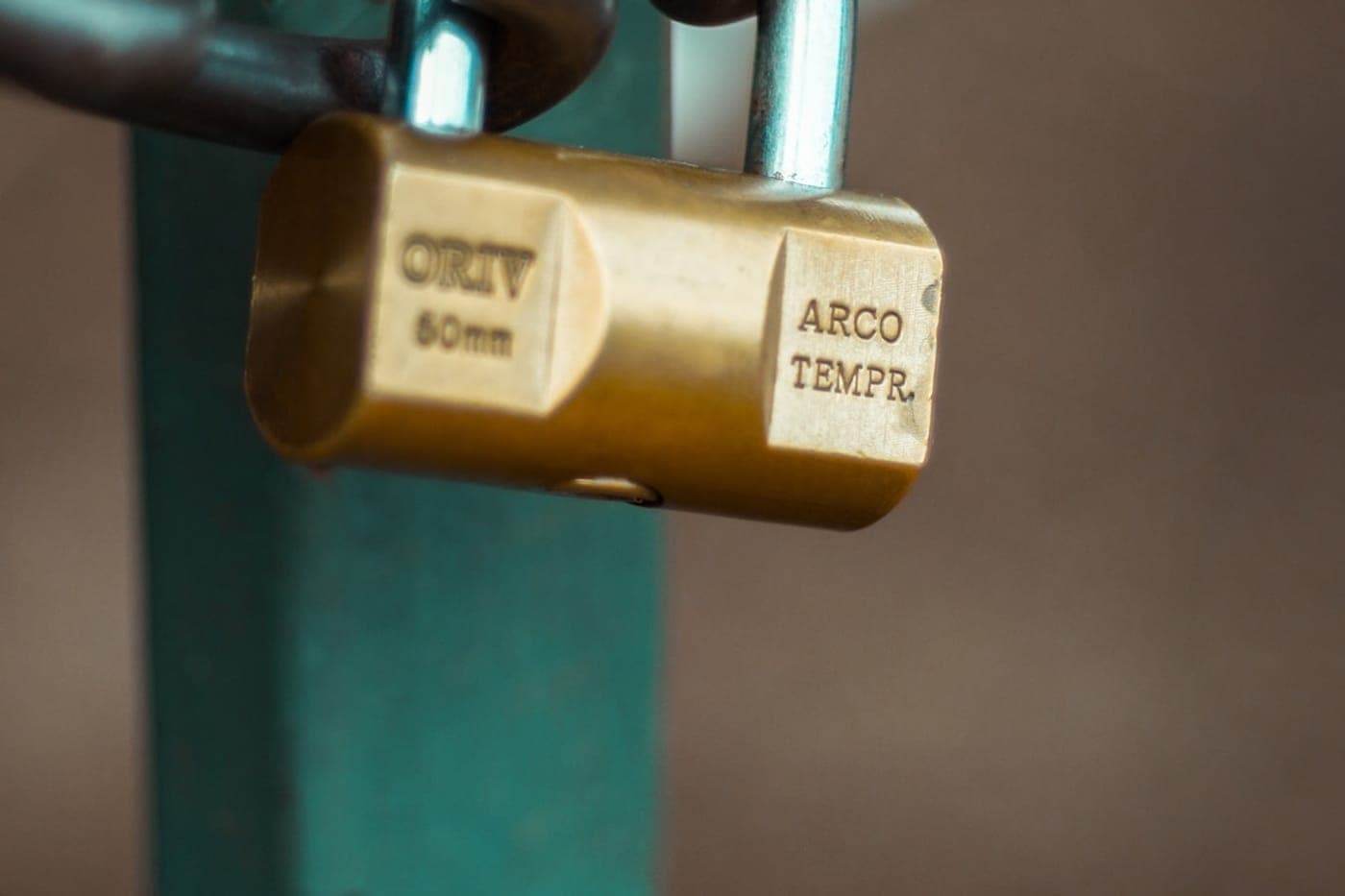 A real brass padlock on a chain against a teal-green post
