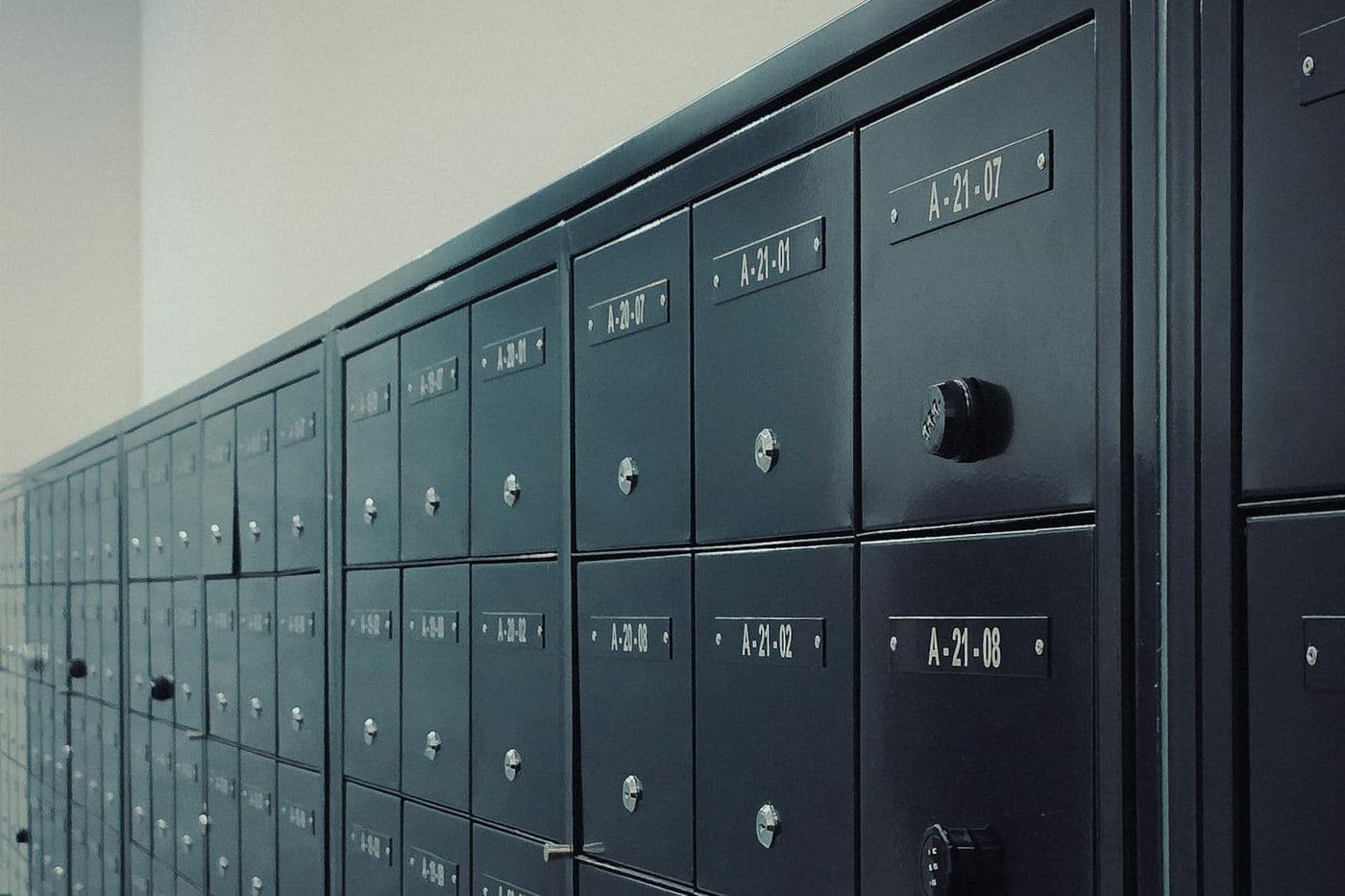 Perspective row of dark metal numbered mailboxes along a wall