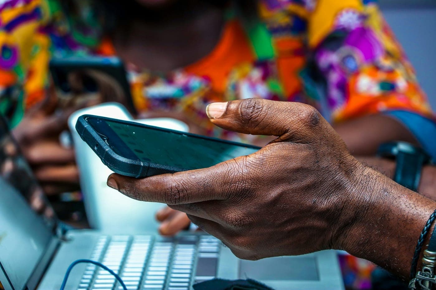 A hand holding a smartphone in Lagos, Nigeria, with a laptop nearby