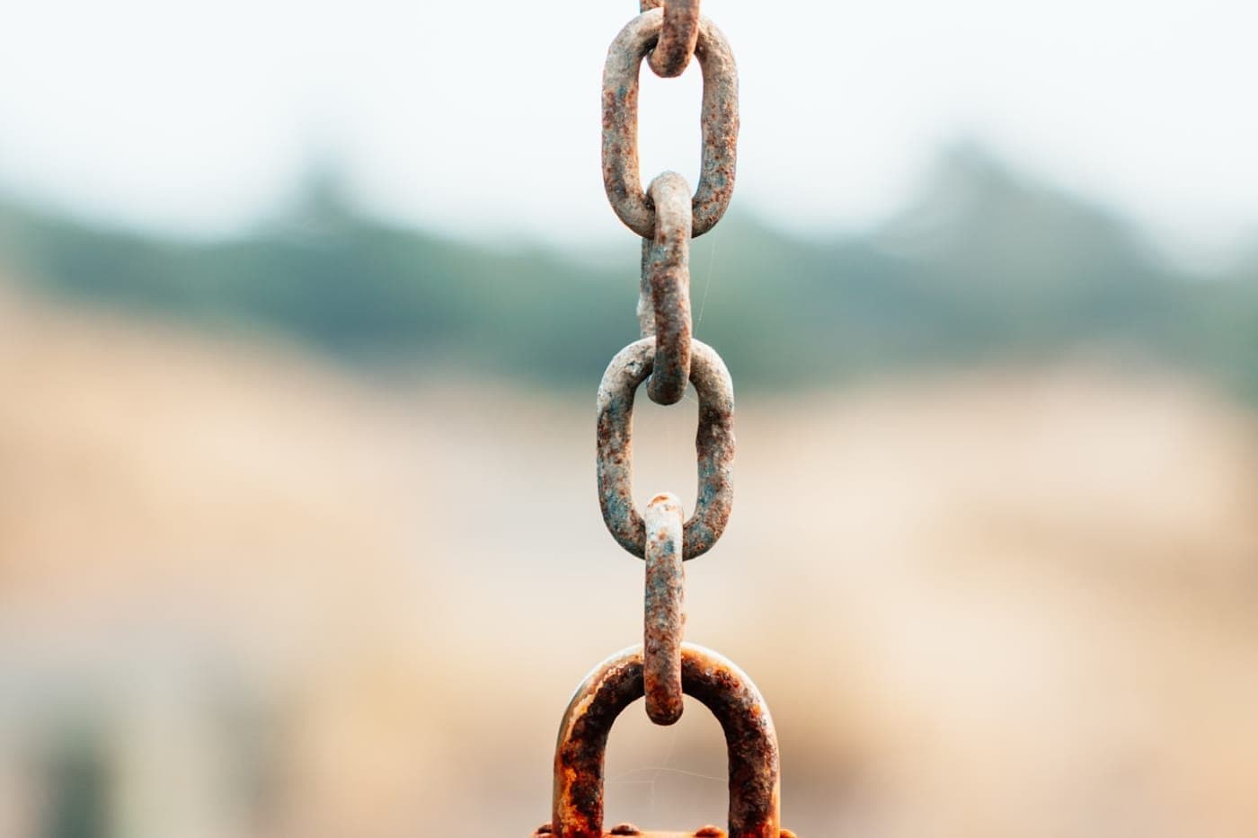 A rusted metal chain ending in a padlock against a soft warm out-of-focus background