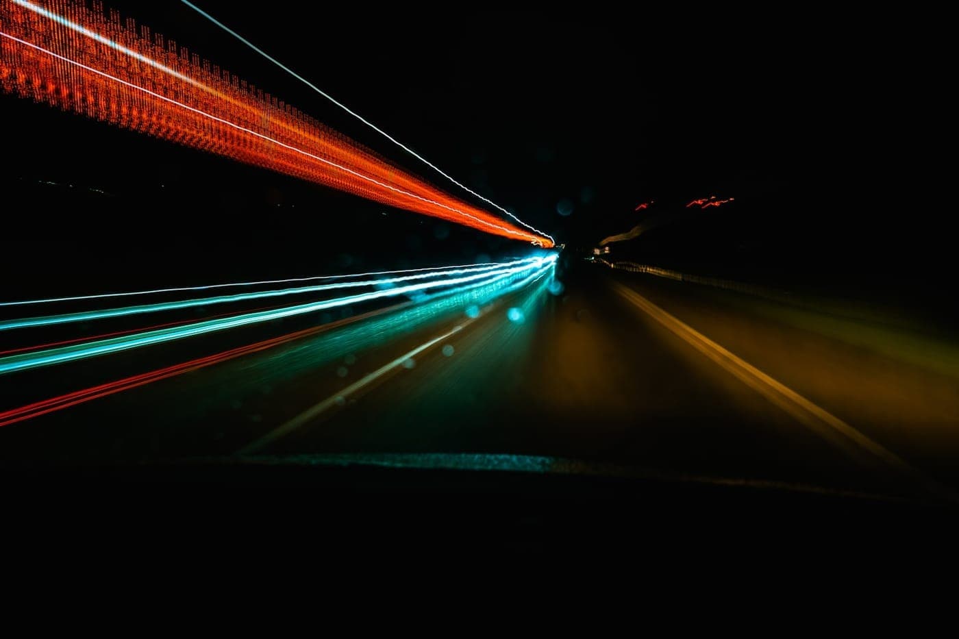 Long-exposure light trails streaking down a dark night highway, conveying speed and motion